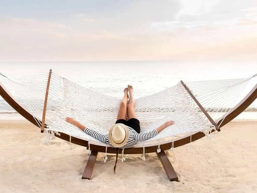 Reiziger in een hangmat aan het strand bij zonsondergang